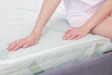 Photo of Woman touching soft mattress on bed indoors, closeup