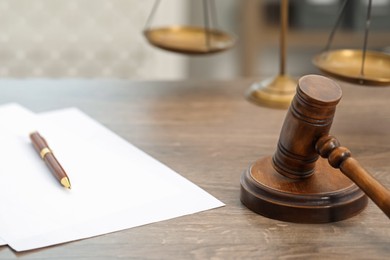 Photo of Papers, judge's gavel and scales on wooden table in office, closeup