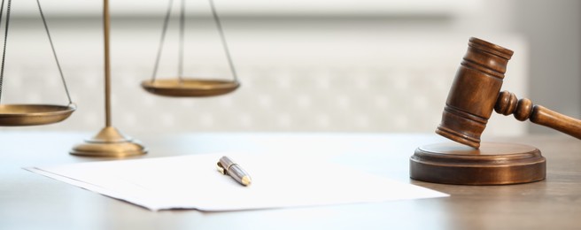 Photo of Papers, judge's gavel and scales on wooden table in office, closeup
