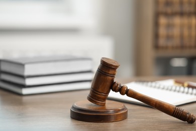 Photo of Judge's gavel, books and notebook on wooden table in office, closeup