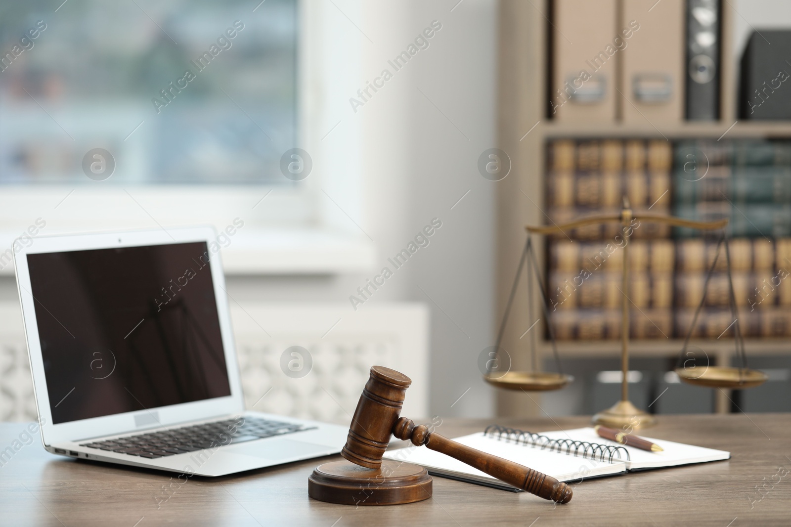 Photo of Laptop, judge's gavel and notebook on wooden table in office
