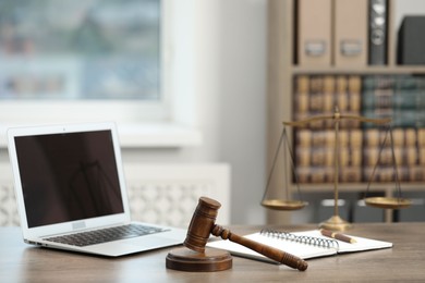 Photo of Laptop, judge's gavel and notebook on wooden table in office