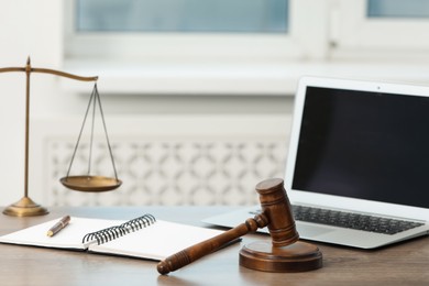 Photo of Laptop, judge's gavel and scales on wooden table in office