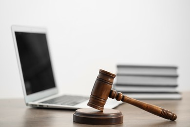 Photo of Laptop, judge's gavel and books on wooden table in office, closeup