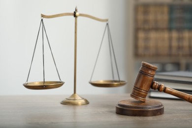 Photo of Judge's gavel, books and scales on wooden table in office, closeup