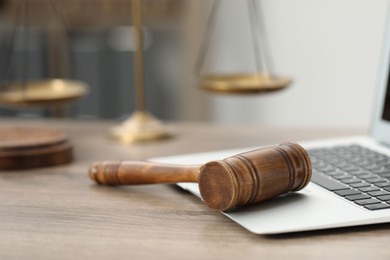 Photo of Laptop, judge's gavel and scales on wooden table in office, closeup