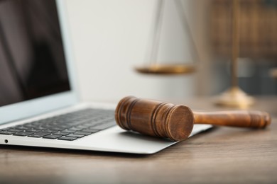 Photo of Laptop, judge's gavel and scales on wooden table in office, closeup