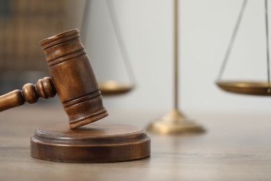 Photo of Judge's gavel and scales on wooden table in office, closeup