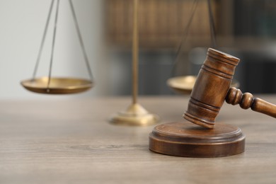 Photo of Judge's gavel and scales on wooden table in office, closeup