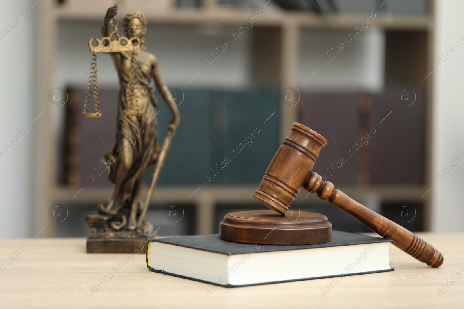 Photo of Judge's gavel, statue and book on wooden table in office, closeup