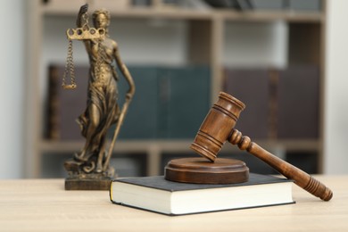 Photo of Judge's gavel, statue and book on wooden table in office, closeup