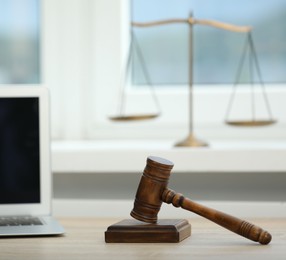 Photo of Laptop, judge's gavel and scales on wooden table in office