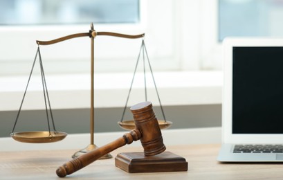 Photo of Laptop, judge's gavel and scales on wooden table in office