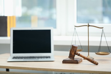 Photo of Laptop, judge's gavel and scales on wooden table in office
