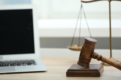 Photo of Laptop, judge's gavel and scales on wooden table in office, closeup