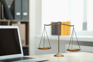 Photo of Judge's workplace with laptop and scales on wooden table in office, closeup