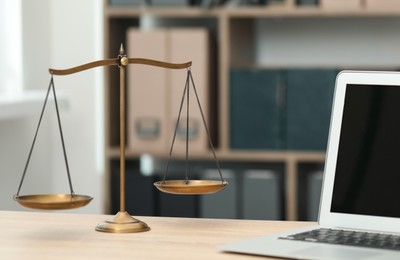 Photo of Judge's workplace with laptop and scales on wooden table in office, closeup
