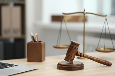 Photo of Laptop, judge's gavel and scales on wooden table in office