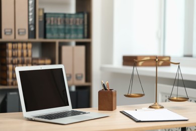 Photo of Judge's workplace with laptop, stationery and scales on wooden table in office