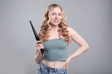 Photo of Woman with beautiful hair and curling iron on grey background
