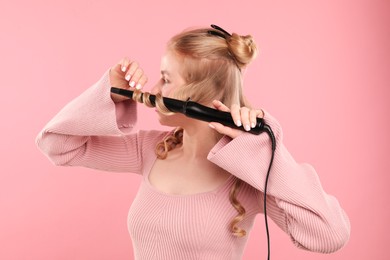 Photo of Woman curling her hair on pink background