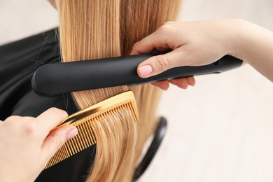 Photo of Hairdresser straightening woman's hair in salon, closeup