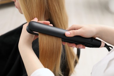 Photo of Hairdresser straightening woman's hair in salon, closeup