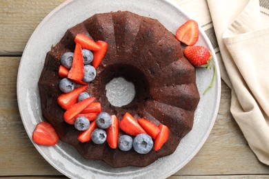 Photo of Tasty chocolate bundt cake with berries on wooden table, top view