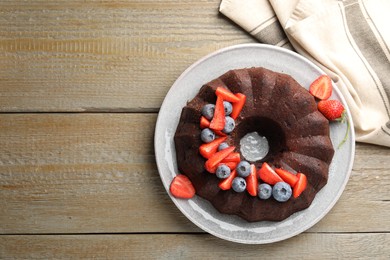Photo of Tasty chocolate bundt cake with berries on wooden table, top view. Space for text