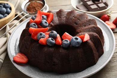 Photo of Tasty chocolate bundt cake with berries on wooden table, closeup