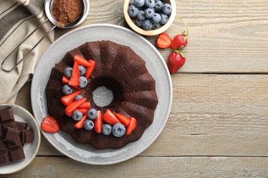 Photo of Tasty chocolate bundt cake with berries on wooden table, flat lay