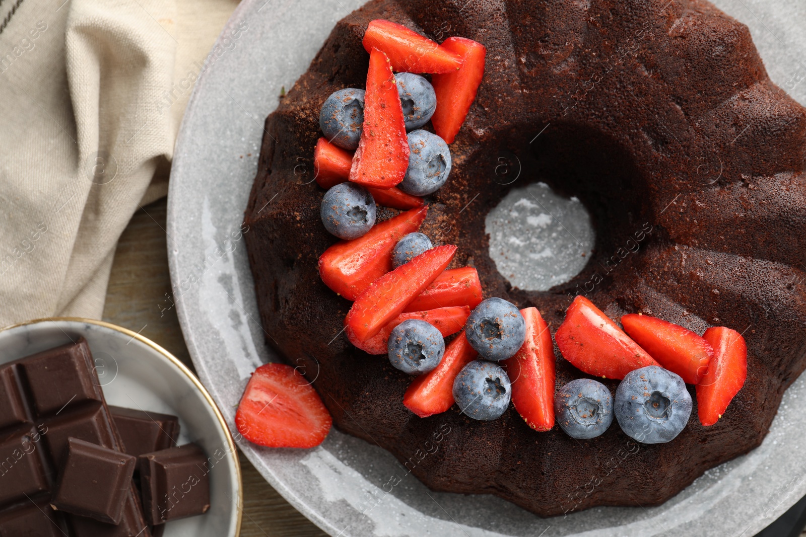 Tasty chocolate bundt cake with berries on wooden table, flat lay Photo of Tasty chocolate bundt cake with berries on wooden table, flat lay