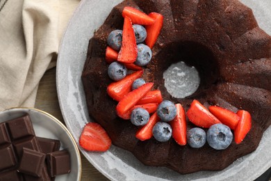 Photo of Tasty chocolate bundt cake with berries on wooden table, flat lay