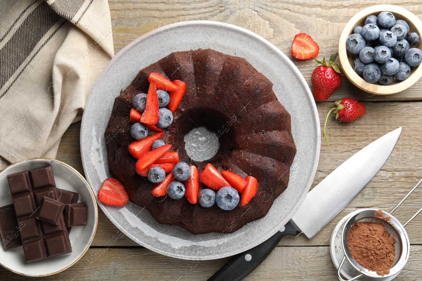 Tasty chocolate bundt cake with berries and knife on wooden table, flat lay Photo of Tasty chocolate bundt cake with berries and knife on wooden table, flat lay