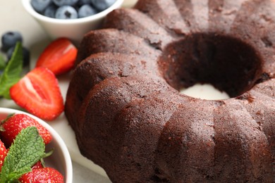 Photo of Tasty chocolate bundt cake and berries on light table, closeup