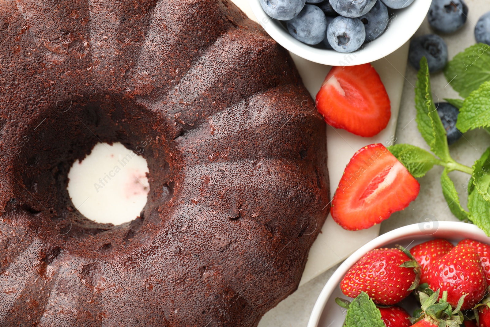 Tasty chocolate bundt cake and berries on light table, flat lay Photo of Tasty chocolate bundt cake and berries on light table, flat lay