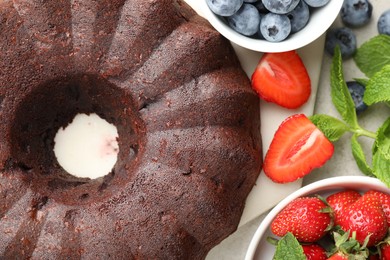 Photo of Tasty chocolate bundt cake and berries on light table, flat lay