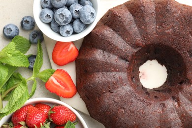 Photo of Tasty chocolate bundt cake and berries on light table, flat lay