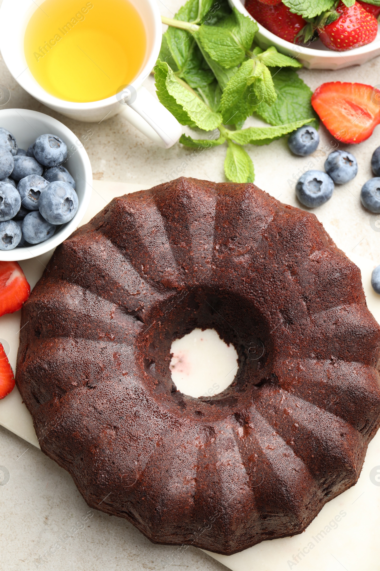 Tasty chocolate bundt cake, tea and berries on light table, flat lay Photo of Tasty chocolate bundt cake, tea and berries on light table, flat lay