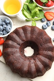 Photo of Tasty chocolate bundt cake, tea and berries on light table, flat lay