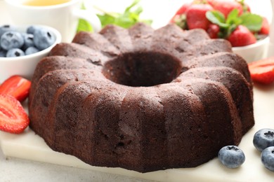 Photo of Tasty chocolate bundt cake and berries on light table, closeup