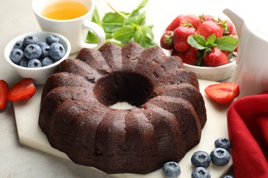 Photo of Tasty chocolate bundt cake, tea and berries on light table, closeup