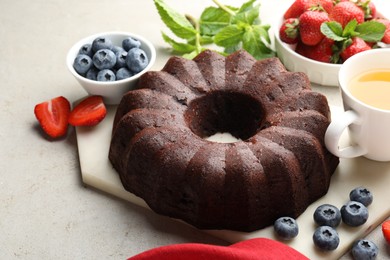 Photo of Tasty chocolate bundt cake, tea and berries on light table, closeup