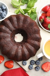 Photo of Tasty chocolate bundt cake, tea and berries on light table, flat lay