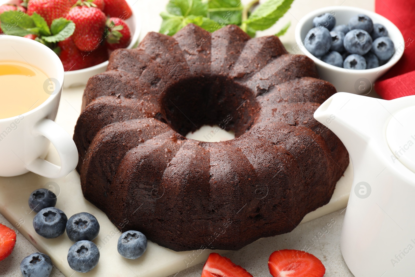 Tasty chocolate bundt cake, tea and berries on light table, closeup Photo of Tasty chocolate bundt cake, tea and berries on light table, closeup