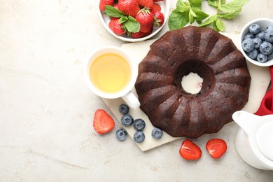 Photo of Tasty chocolate bundt cake, tea and berries on light table, flat lay. Space for text