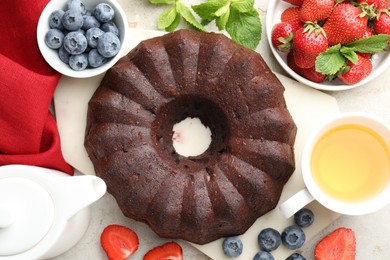 Photo of Tasty chocolate bundt cake, tea and berries on light table, flat lay