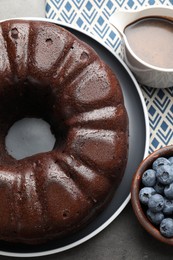 Photo of Tasty chocolate bundt cake and blueberries on grey table, top view