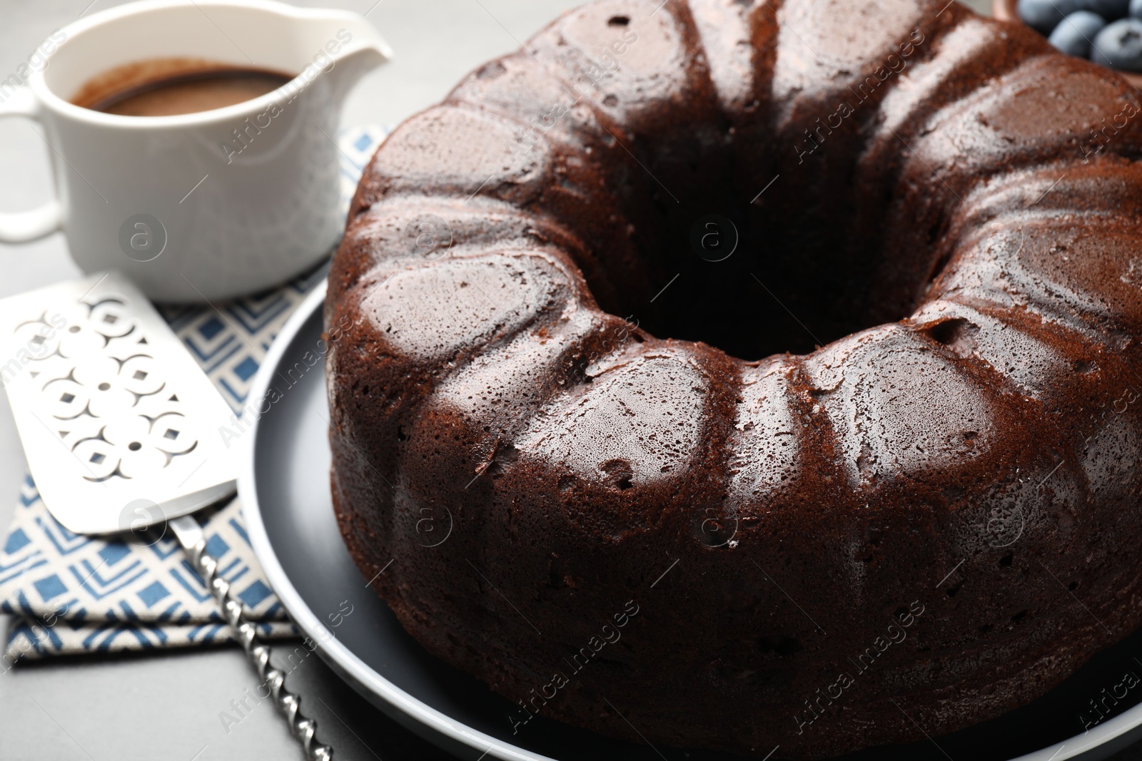 Tasty chocolate bundt cake and server on grey table, closeup Photo of Tasty chocolate bundt cake and server on grey table, closeup