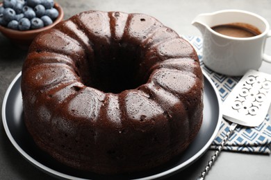 Photo of Tasty chocolate bundt cake, blueberries and server on grey table, closeup